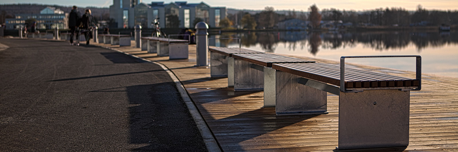 Benches line a walkway next to a scenic lake at sunset.